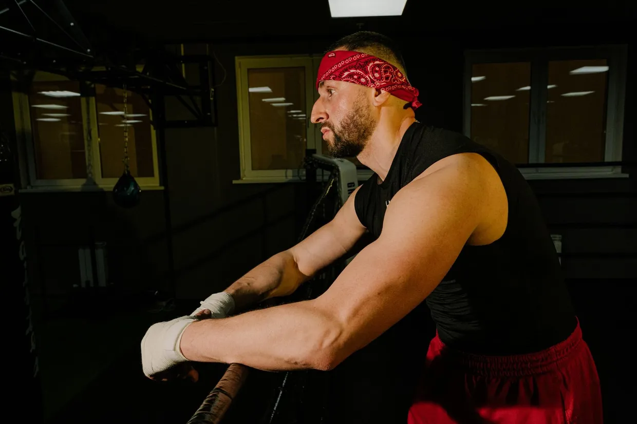 Boxeador con las manos vendadas apoyado en las cuerdas del ring, recuperando el aliento en el gimnasio