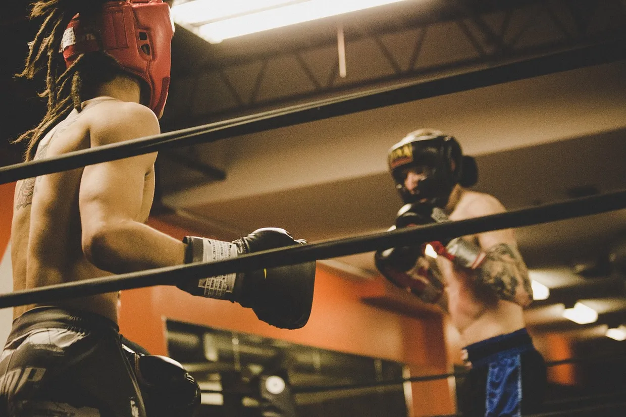Dos boxeadores con casco guanteando en el ring de un gimnasio