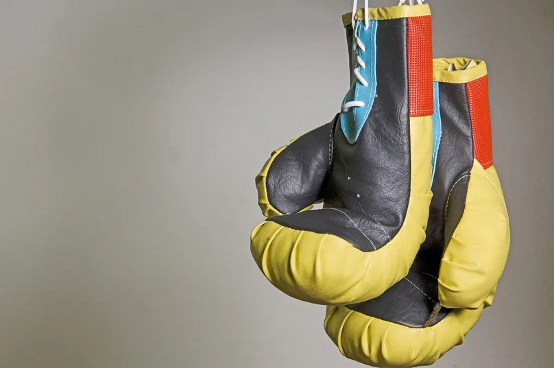 Dos guantes de boxeo amarillos y negros colgados por los cordones delante de una pared gris