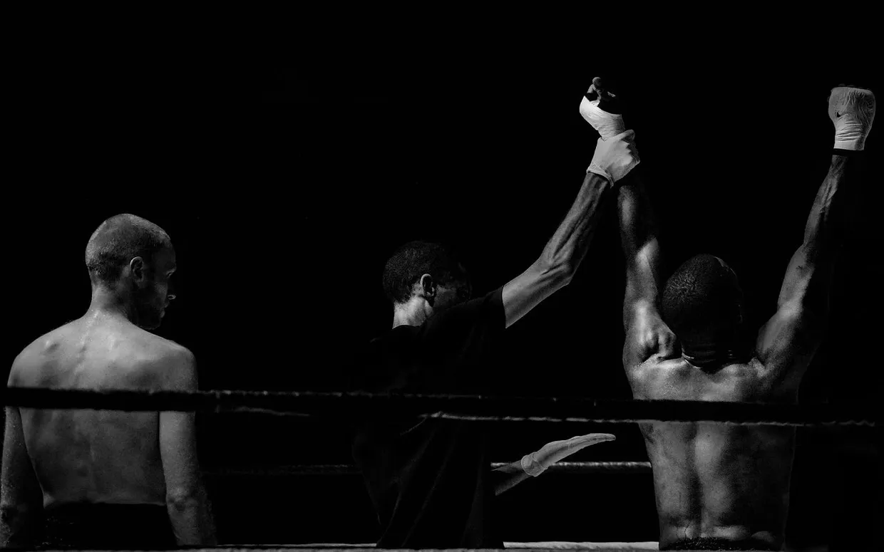 El árbitro levanta el brazo del boxeador ganador en el ring, en blanco y negro, mientras el otro espera de espaldas