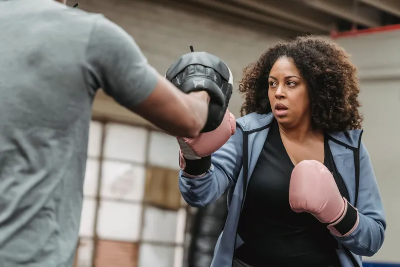 Mujer con guantes de boxeo golpeando la manopla que le sujeta su entrenador en un gimnasio