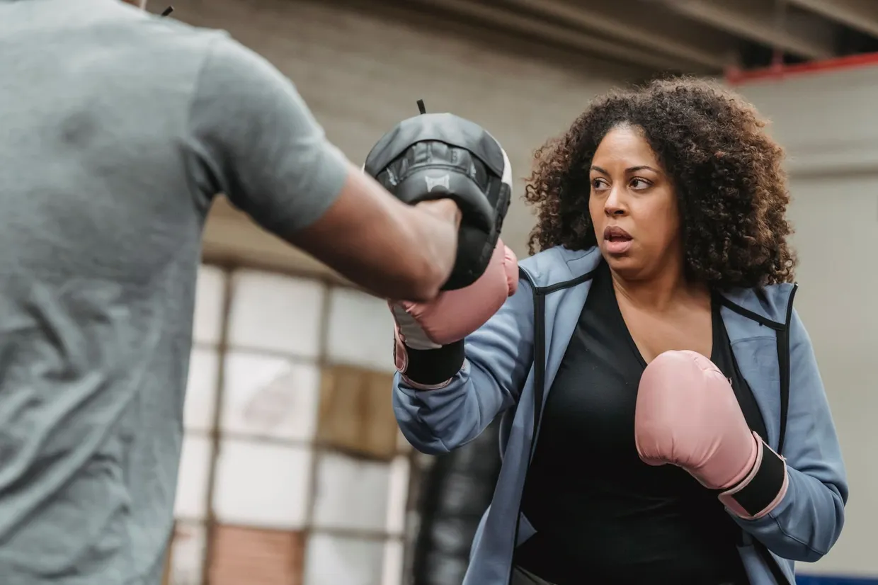 Mujer con guantes de boxeo golpeando la manopla que le sujeta su entrenador en un gimnasio