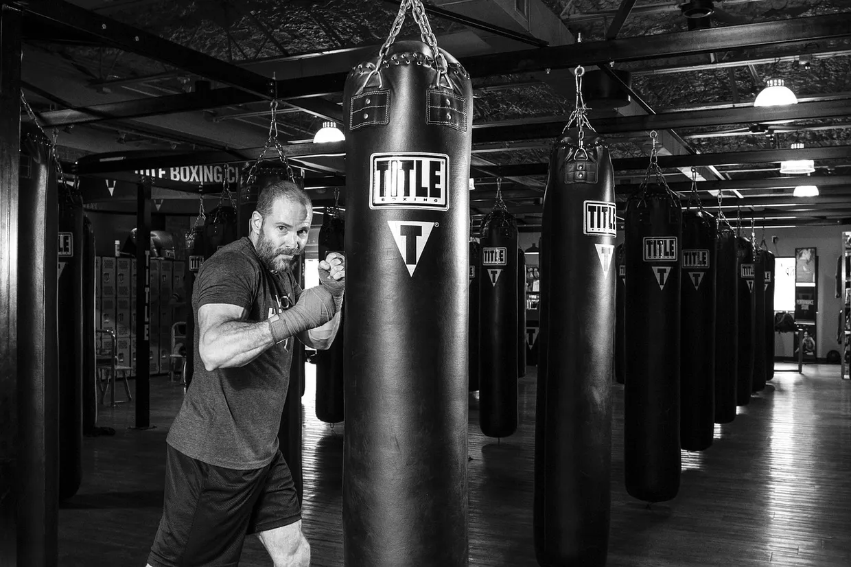 Hombre entrenando boxeo frente a una fila de sacos en un gimnasio