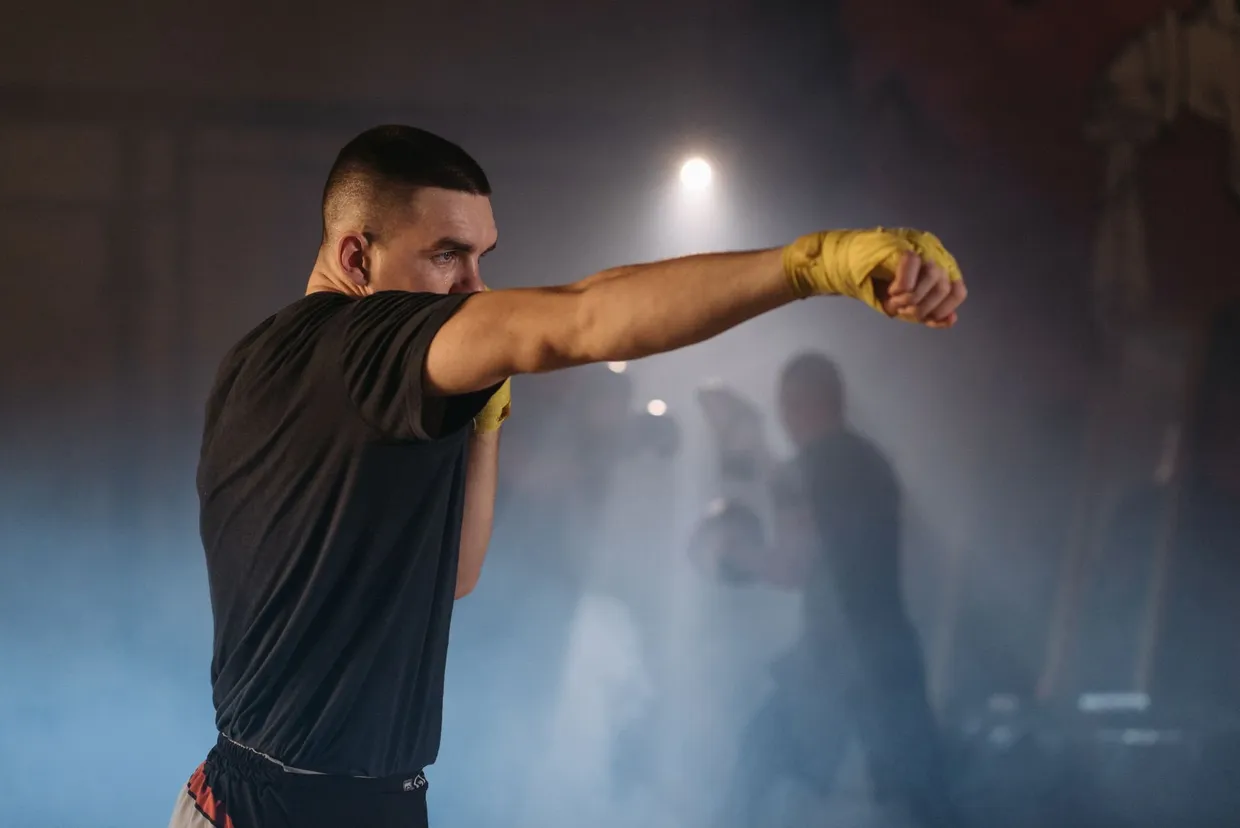 Boxeador con las manos vendadas lanzando un golpe recto al aire en un gimnasio en penumbra